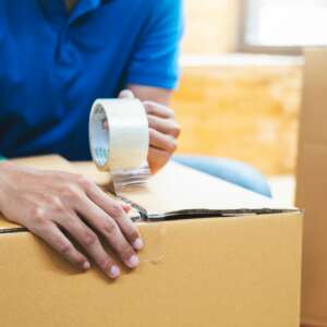 Delivery man packing cardboard box using tape dispenser .